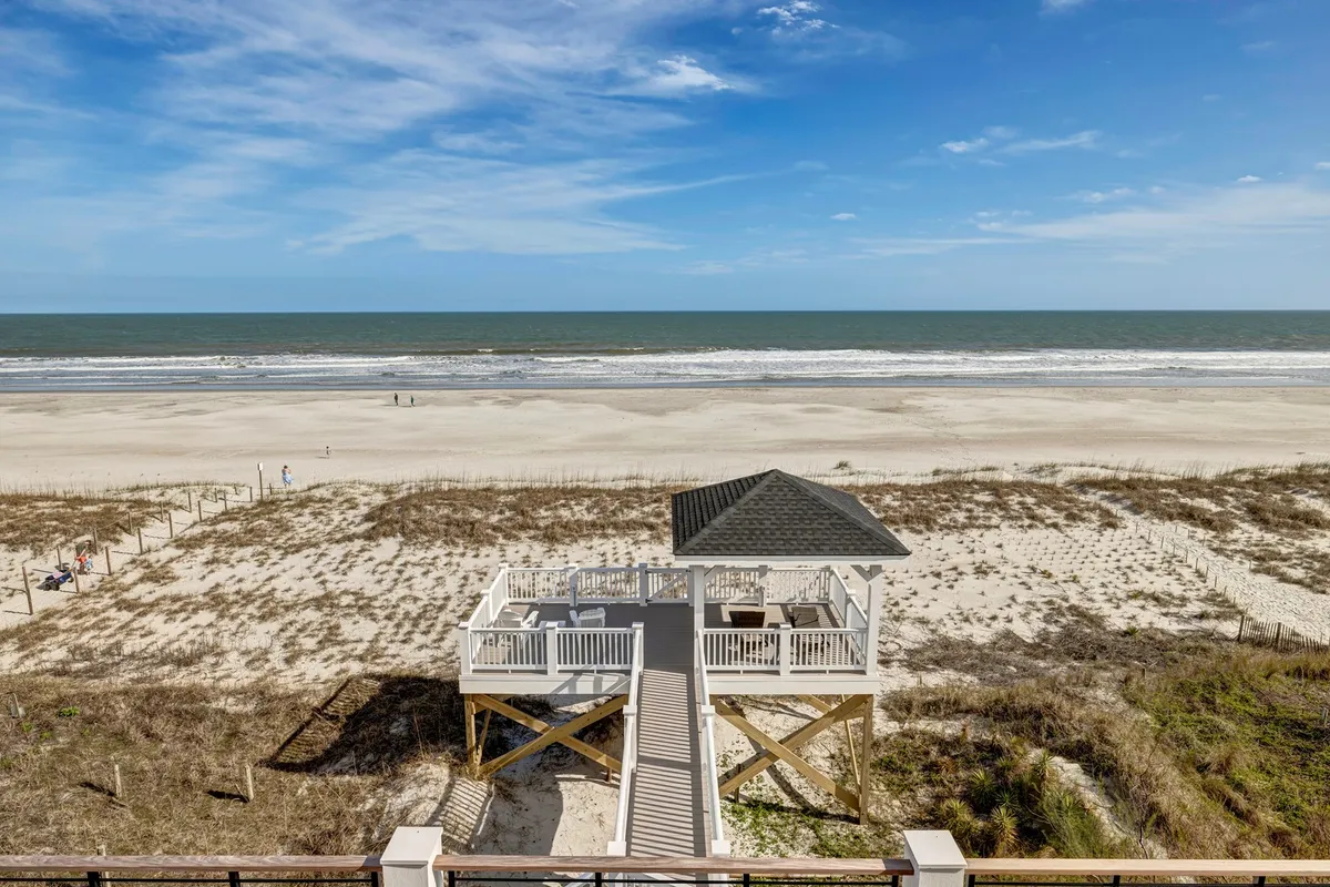 A relaxed beachfront scene featuring a charming gazebo overlooking sandy shores, with gentle ocean waves in the background and distant beachgoers enjoying a day by the sea. The setting is inviting for families looking to explore, picnic, or simply unwind by the water.