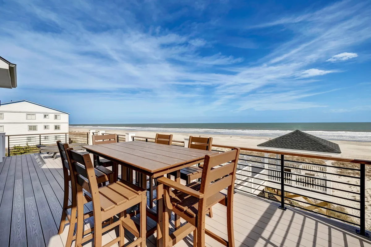 A breezy exterior setting featuring an outdoor dining table set against a sweeping ocean backdrop, under an open sky. The arrangement suggests alfresco meals, sunset barbecues, and group gatherings with water views.