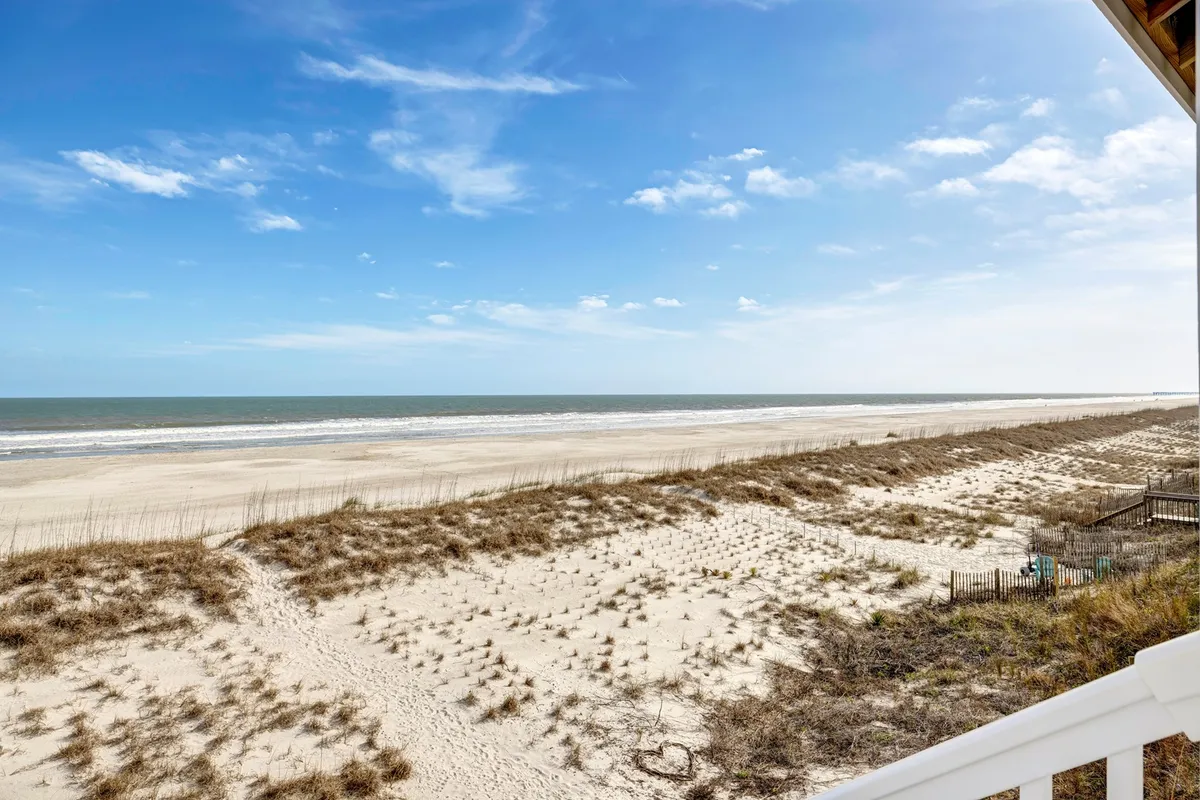A wide expanse of beach stretches out towards the gentle waves and distant horizon, with dune grasses framing the scene. The atmosphere is serene, inviting families and pet owners to beachcomb, build sandcastles, or enjoy the sunrise over the ocean.