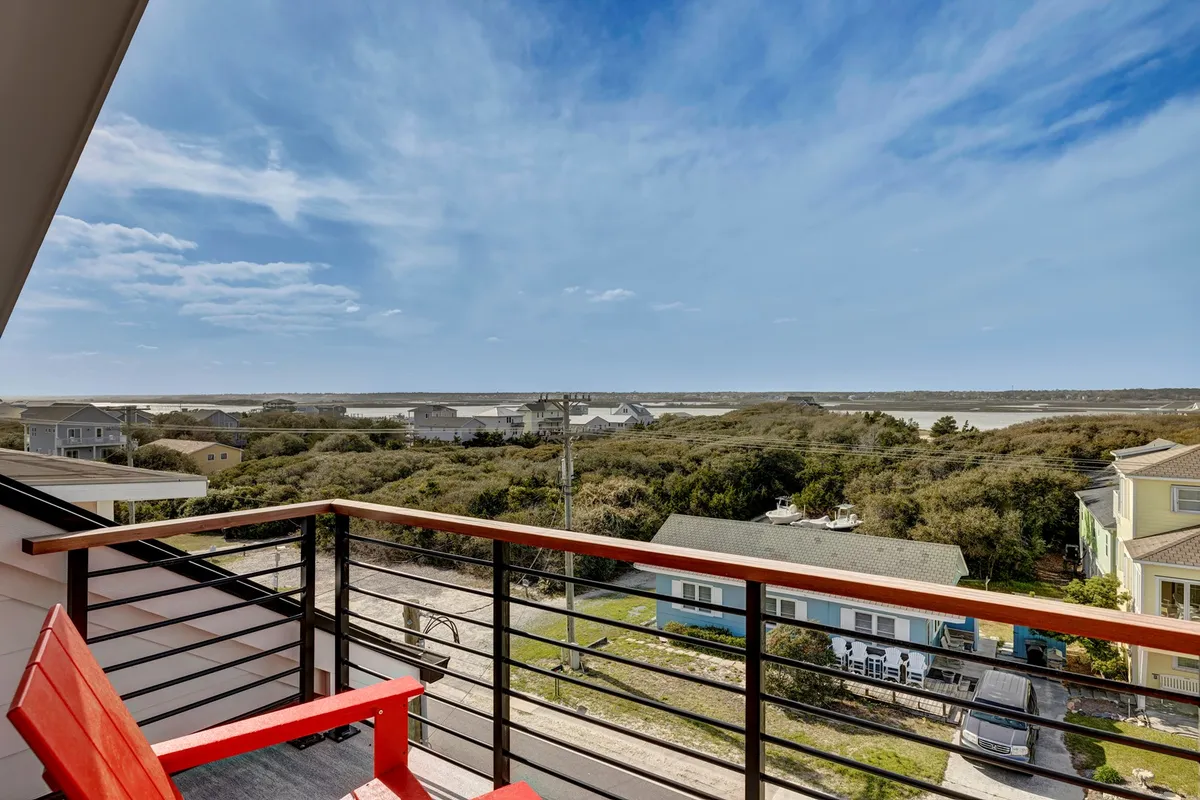 A tranquil balcony scene with a single red chair facing an expansive view of the landscape, distant houses, and open sky. The setting evokes a sense of solitude—perfect for quiet moments like morning coffee, reading, or sunset watching from a private retreat above it all.