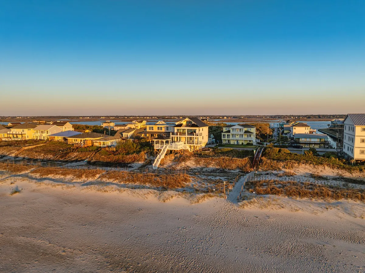 A row of beachfront homes nestled along sandy dunes, with an expansive ocean view in the background. The setting is tranquil, inviting, and clearly communicates the context of a well-managed, welcoming vacation environment.