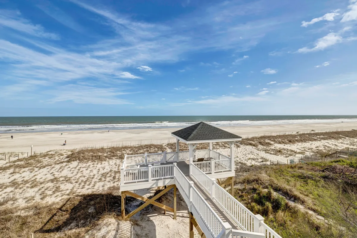 A scenic view of a sand dune and a pet-friendly beach access gazebo, with the ocean sparkling in the background. The scene is relaxed, welcoming, and ideal for families and dog owners seeking easy, picturesque entry to the shoreline.