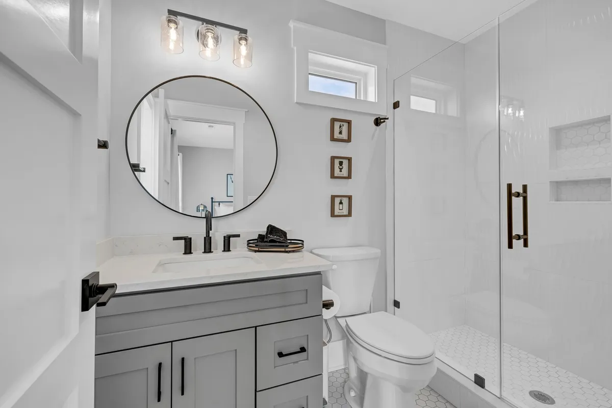 A spa-inspired bath with a round mirror above a modern vanity sink and a glass shower enclosure. The fresh, inviting aesthetic makes it ideal for moments of self-care, reflecting the luxurious bathroom features highlighted in the master suite.