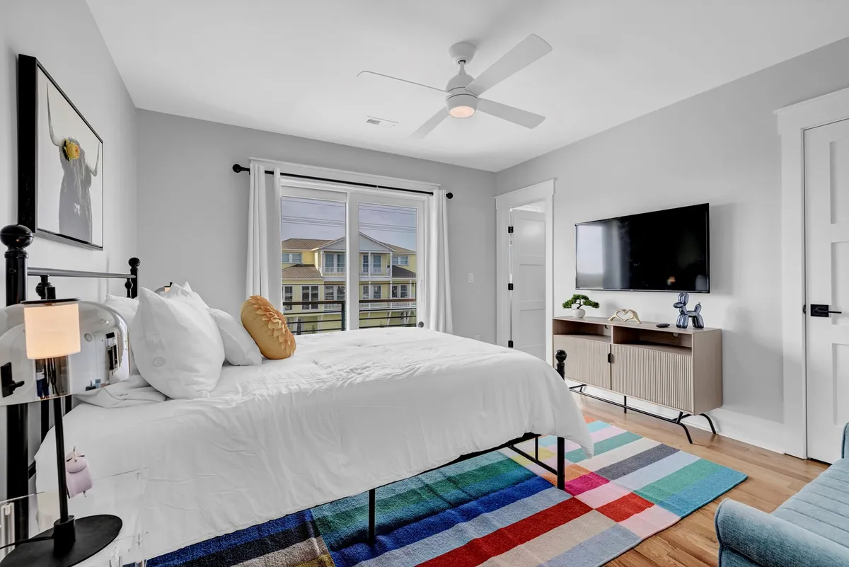A bright, comfortable bedroom featuring a well-made bed, a cozy rug, a TV, and a window letting in daylight. The space feels homey and adaptable, offering a pleasant retreat for any guest—whether family, friends, or those bringing a pet.
