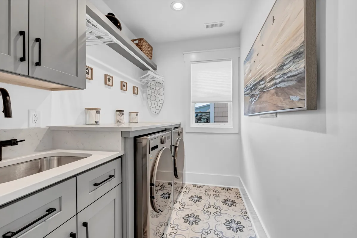 A modern, organized laundry area featuring a washer and dryer, a deep sink, decorative shelving, and tasteful wall art. The space is bright, clean, and designed for both practicality and comfort, supporting longer stays and guest convenience.