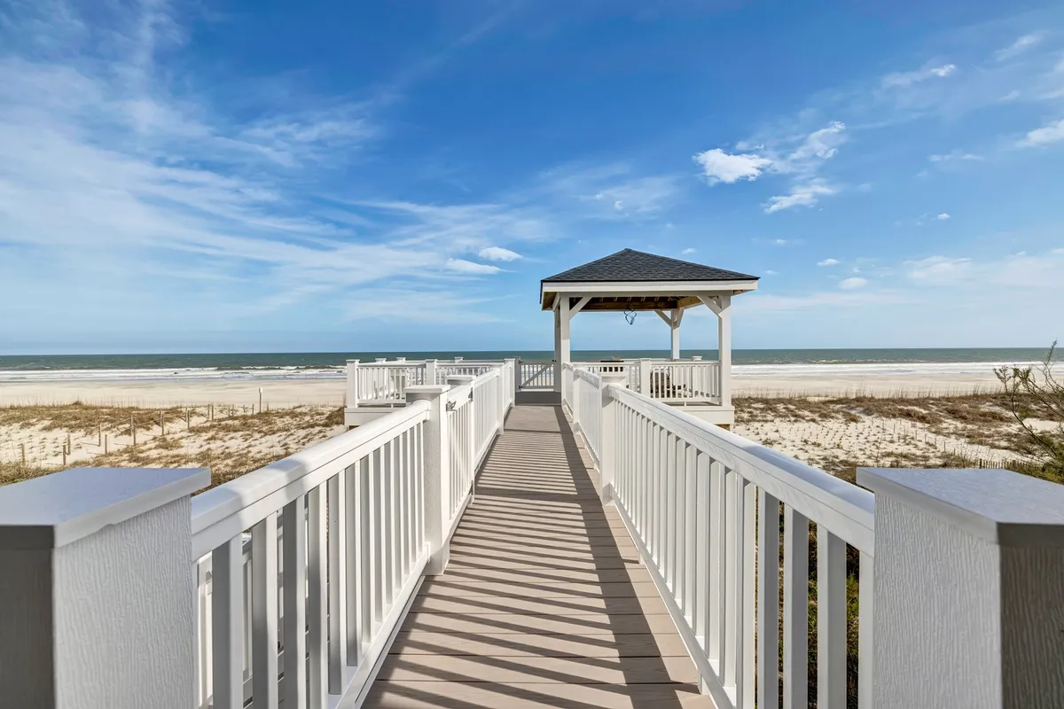 A tranquil exterior scene featuring a charming gazebo overlooking the ocean, with a boardwalk leading guests to the water. The golden hues of sunset bathe the gazebo, inviting leisurely strolls, morning coffee, or relaxing moments while taking in panoramic views.
