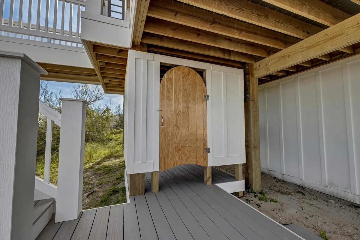 A charming arched wooden door opens onto a wooden deck with a sturdy railing, surrounded by natural greenery. The outdoor transition area is both welcoming and private.